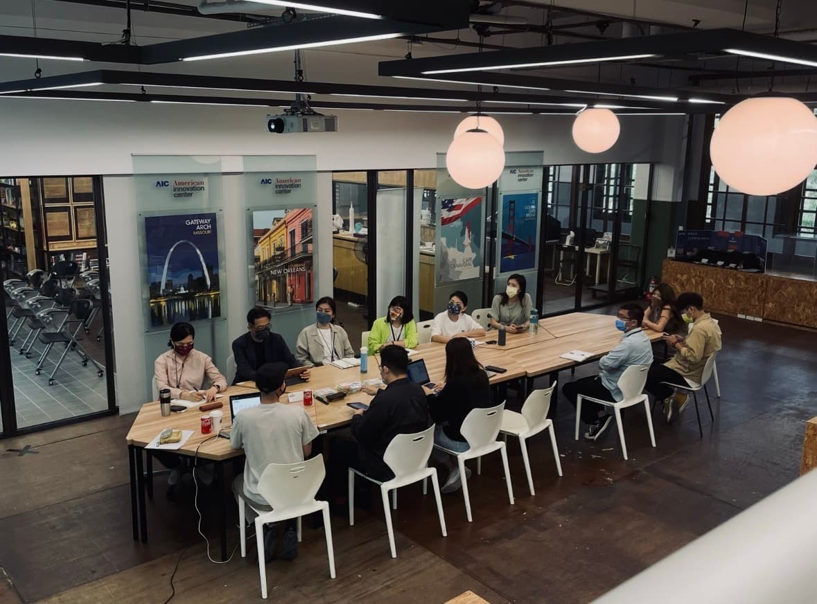 A co-creation workshop for the Songshan sustainability transformation project during my DreamVok internship — around a dozen masked participants seated at a long table, with American Innovation Center city posters on the wall