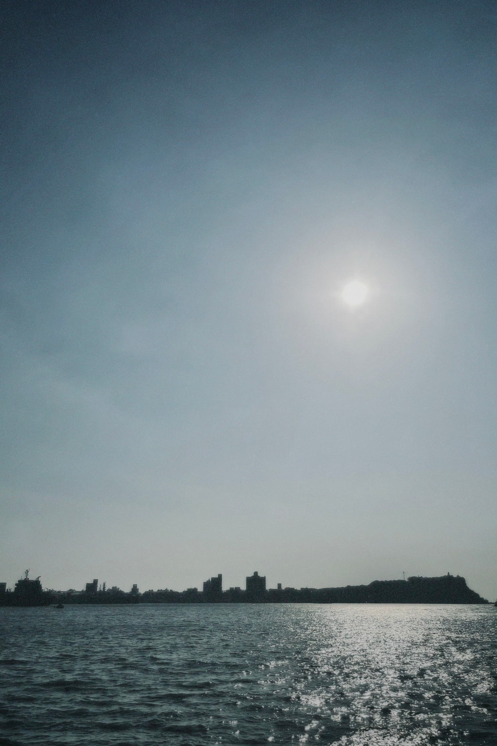 高雄駁二碼頭的逆光海景,太陽映照在水面上,遠方是城市天際線的剪影