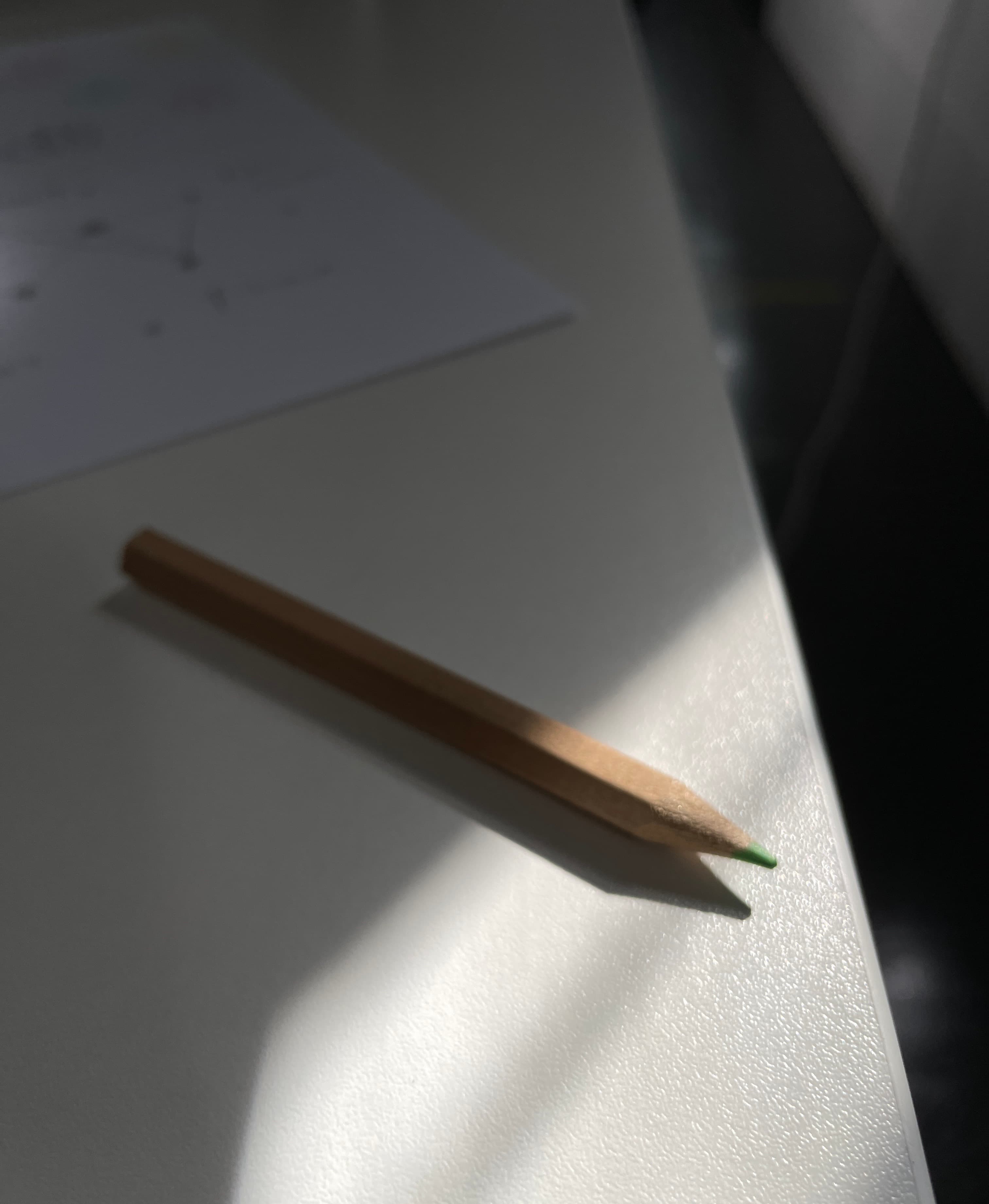 一支削尖的綠色色鉛筆躺在 RCA 工作室的白色桌面上,午後陽光切出長長的影子