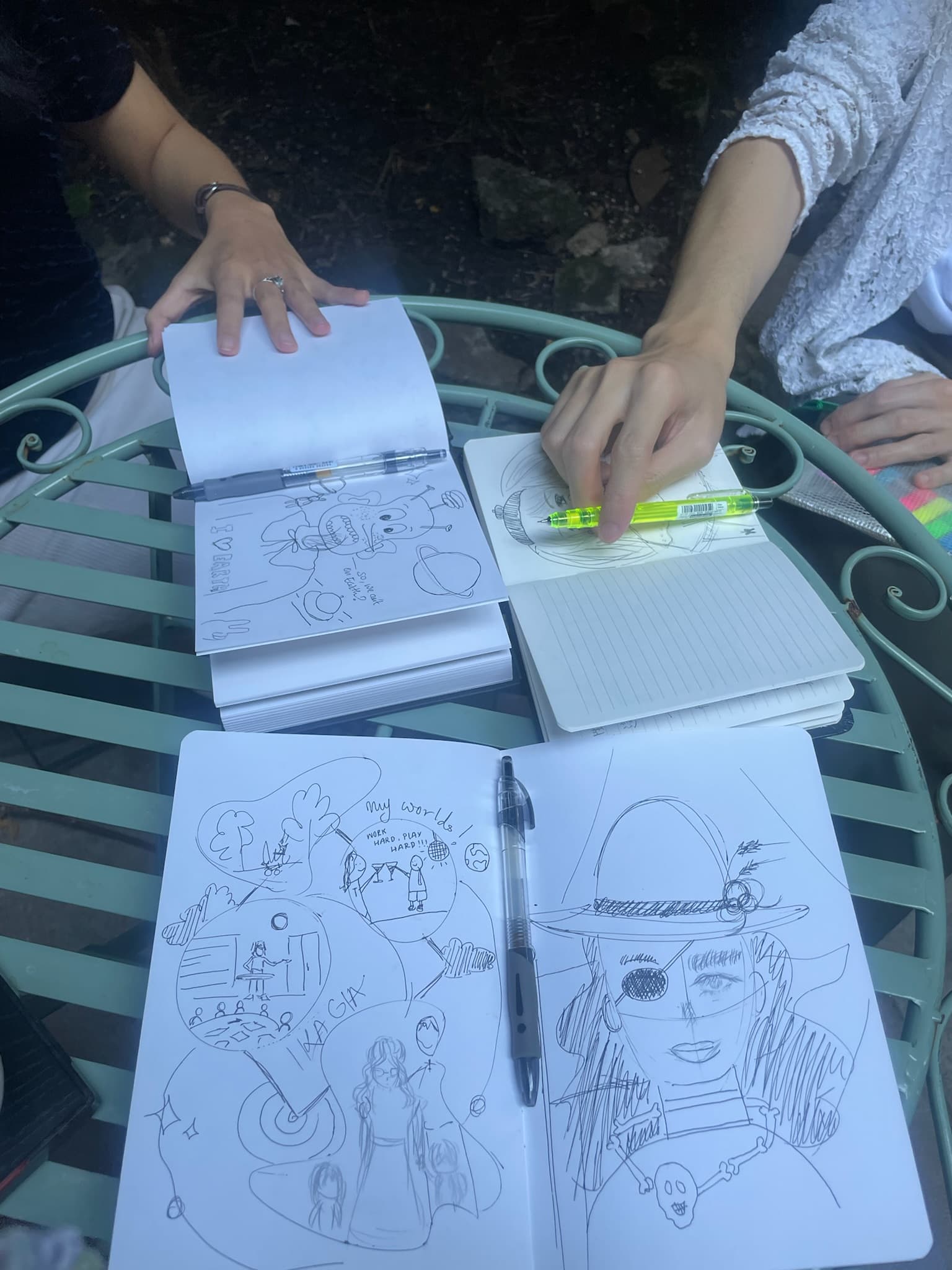 花園鐵桌上攤開三本畫滿草圖與塗鴉的筆記本