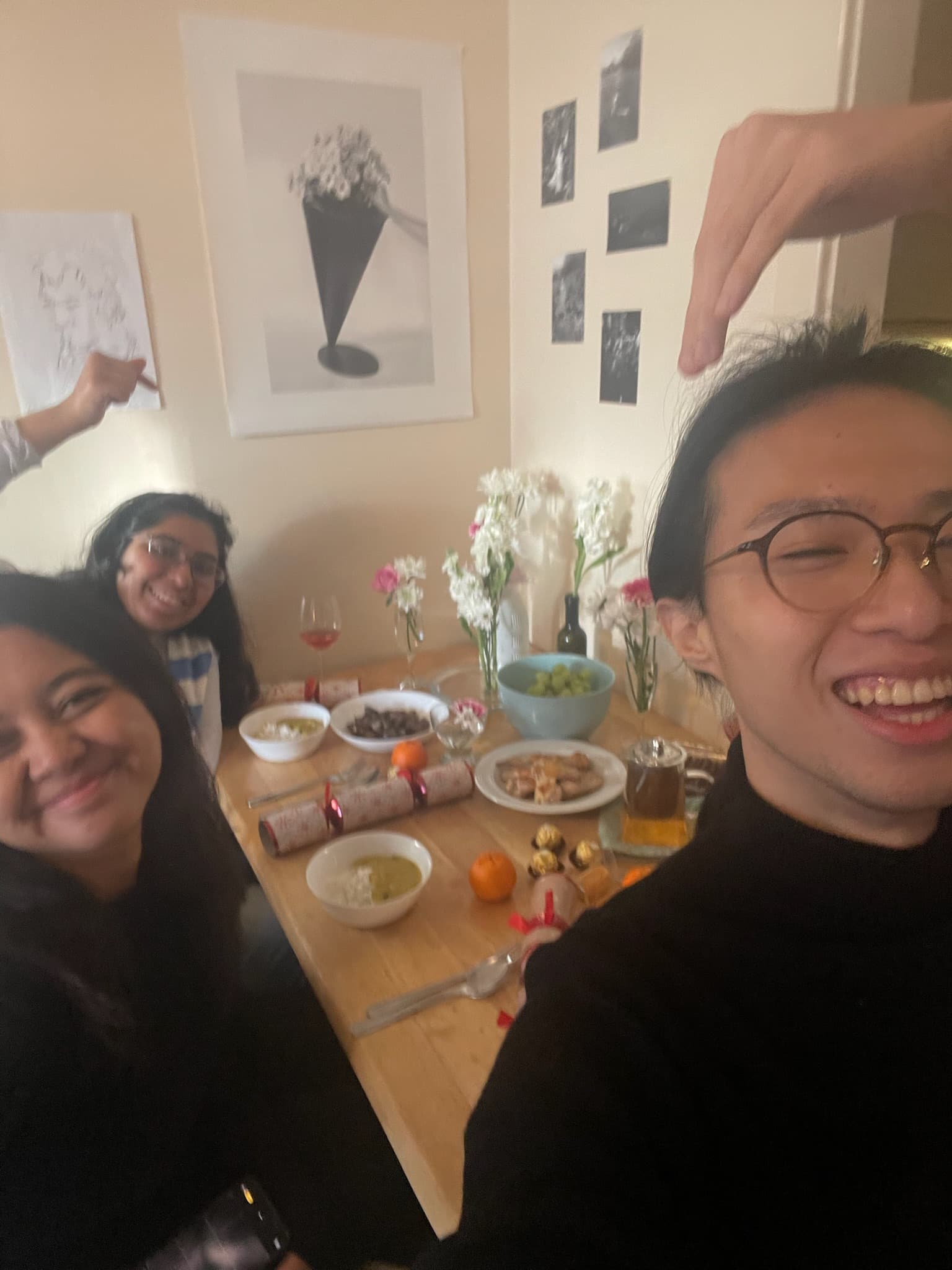三人擠在餐桌前的自拍,桌上擺著聖誕拉炮、小點心和幾瓶插著白花的玻璃瓶