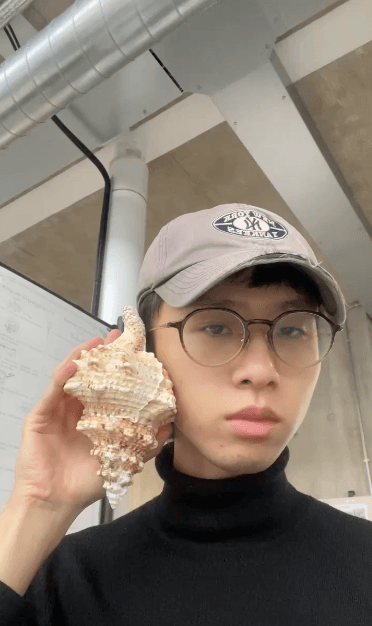 自拍:我戴著帽子和眼鏡、穿黑色高領,把海螺貼在耳邊像在講電話
