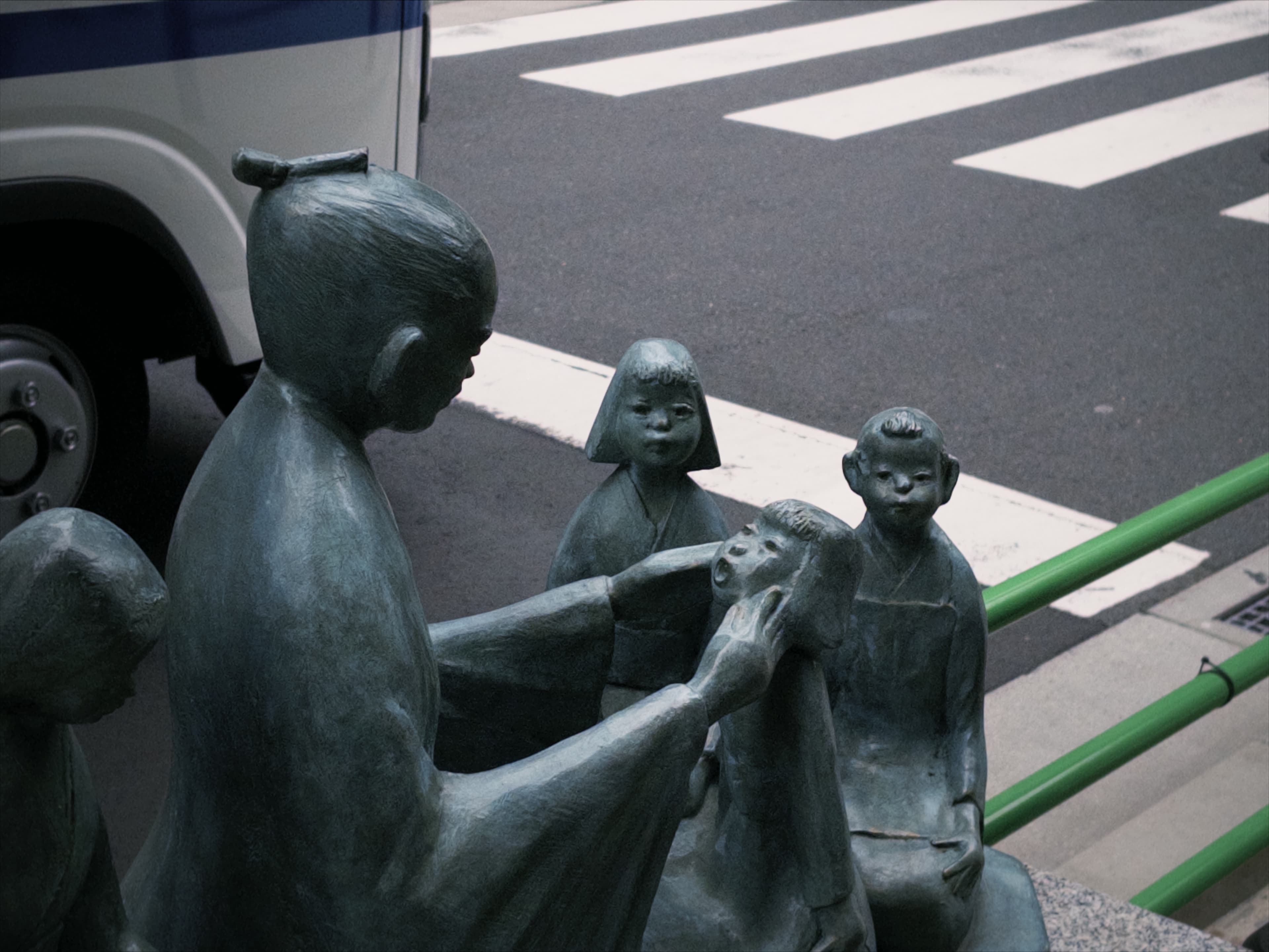 Bronze street sculpture of an adult figure guiding a group of children by the roadside